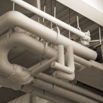 Complex network of industrial pipes and ducts in a sepia-toned indoor setting.